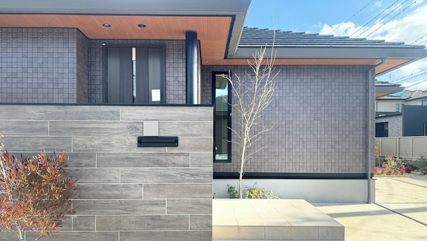 A modern building with a grey tiled facade, a wooden door, and a small tree in the foreground. - Akikawa Miyoshi 1 | 20 min to TSMC | Entire 3LDK House | Up to 6 Guests (Koshi)