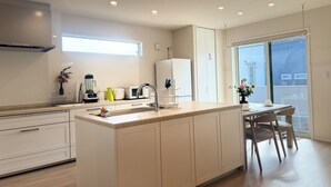 A modern kitchen with a central island, built-in appliances, and a dining area with a view. - Akikawa Miyoshi 1 | 20 min to TSMC | Entire 3LDK House | Up to 6 Guests (Koshi)