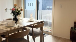 A dining area with a table set for two, a vase with flowers, and a view through a sliding door to the outside. - Akikawa Miyoshi 1 | 20 min to TSMC | Entire 3LDK House | Up to 6 Guests (Koshi)