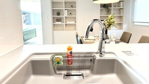 Una cocina moderna con un lavamanos de acero inoxidable, una lámpara colgante negra y una encimera blanca.