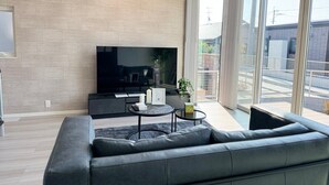 Una sala de estar moderna con un televisor de pantalla plana grande, un sofá gris, una mesita de centro pequeña y un ventanal con vistas al exterior.