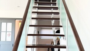 Un interior moderno con una escalera central, barandillas de vidrio y vistas a una habitación con escritorio y silla.