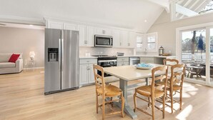 Una cocina moderna con armarios blancos, electrodomésticos de acero inoxidable y una zona de comedor con sillas de madera.