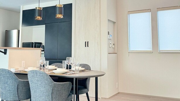Un espace repas moderne avec une table ronde, des chaises à revêtement gris, des luminaires suspendus et une cuisine en arrière-plan.