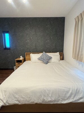 Uma cama bem arrumada com roupa de cama branca, cabeceira de madeira e um único travesseiro azul.