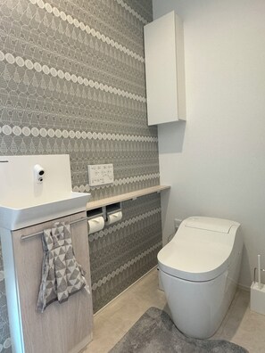 Um banheiro com parede estampada, vaso sanitário, pia e porta-toalhas.