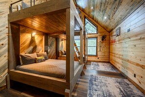 Interior de una cabaña de madera con literas, una ventana pequeña y un aro de baloncesto.