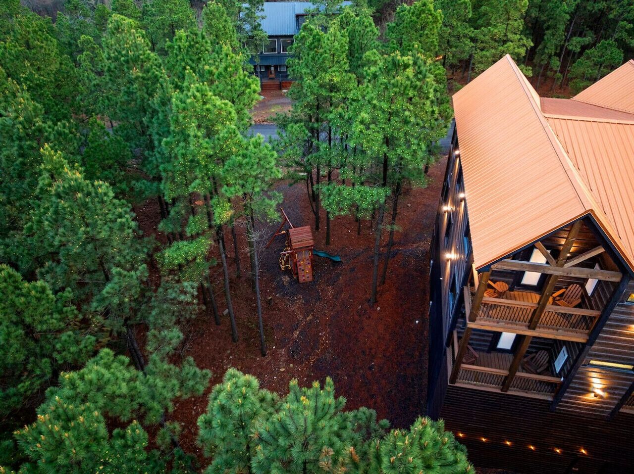 A treehouse with a wooden deck and a metal roof, surrounded by dense forest.