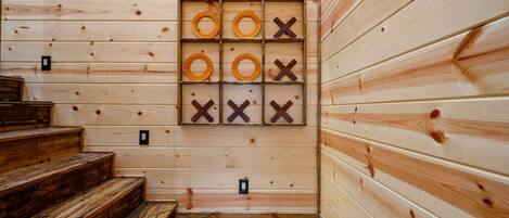 Interior de una cabaña de madera con una escalera de madera, un tablero de juego en la pared y una lámpara.