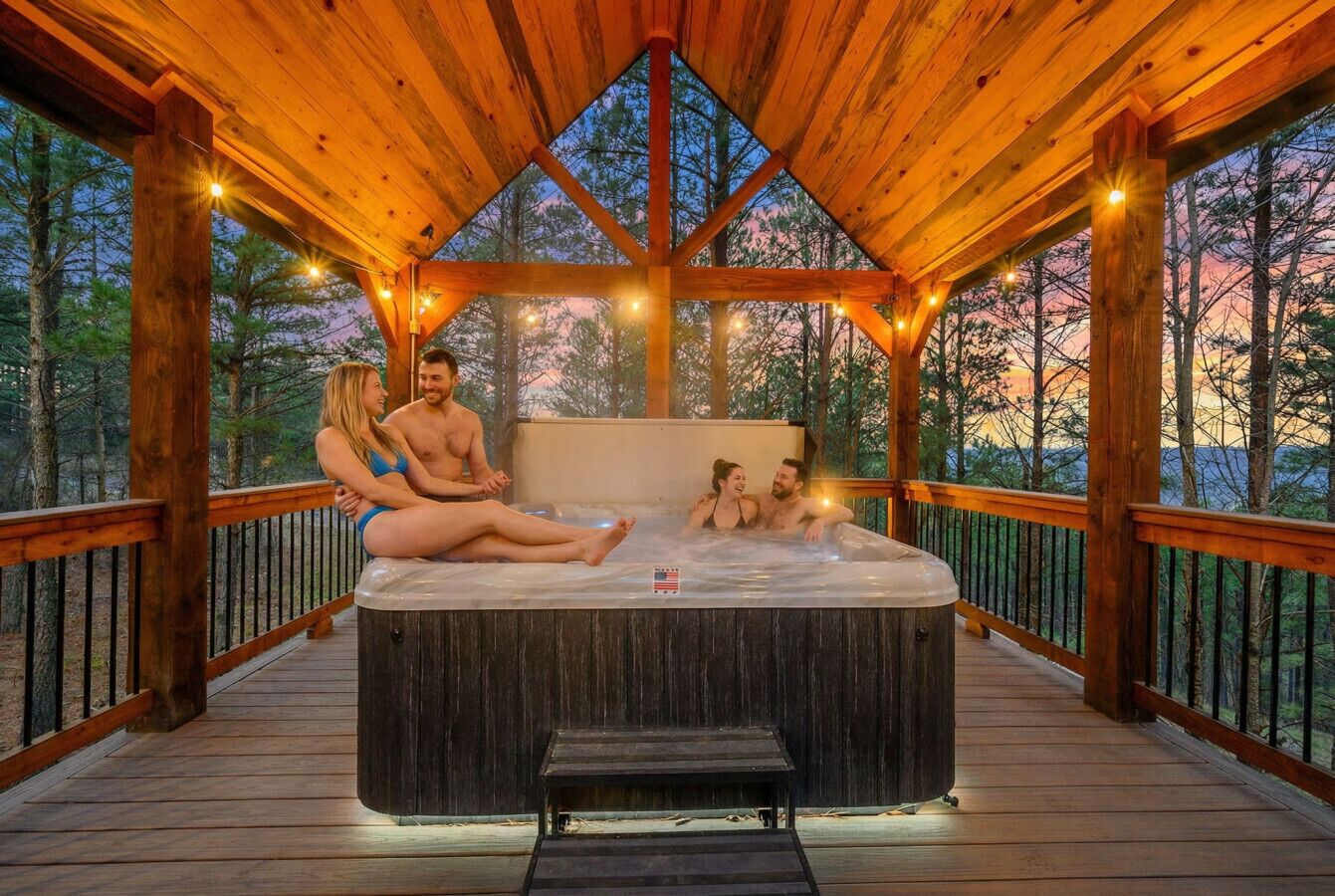 A hot tub with wooden deck and railings, surrounded by trees.