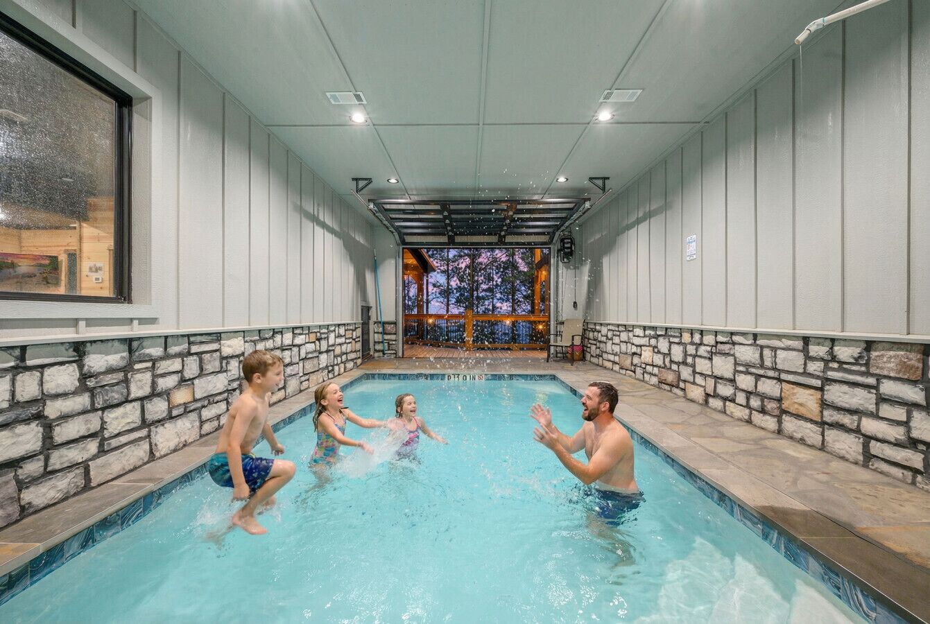 An indoor swimming pool with stone walls and a view of the cityscape through a large window.