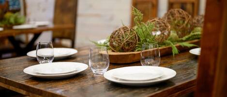 Una mesa de comedor de madera con platos blancos y vasos transparentes, rodeada de decoración rústica que incluye esferas tejidas y follaje.