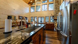 A modern kitchen with a large island, stainless steel appliances, and a stone fireplace. - Swimming Beaver Mansion · Indoor Pool Year-Round, Sleeps 28, Game Room, Views! (Broken Bow)