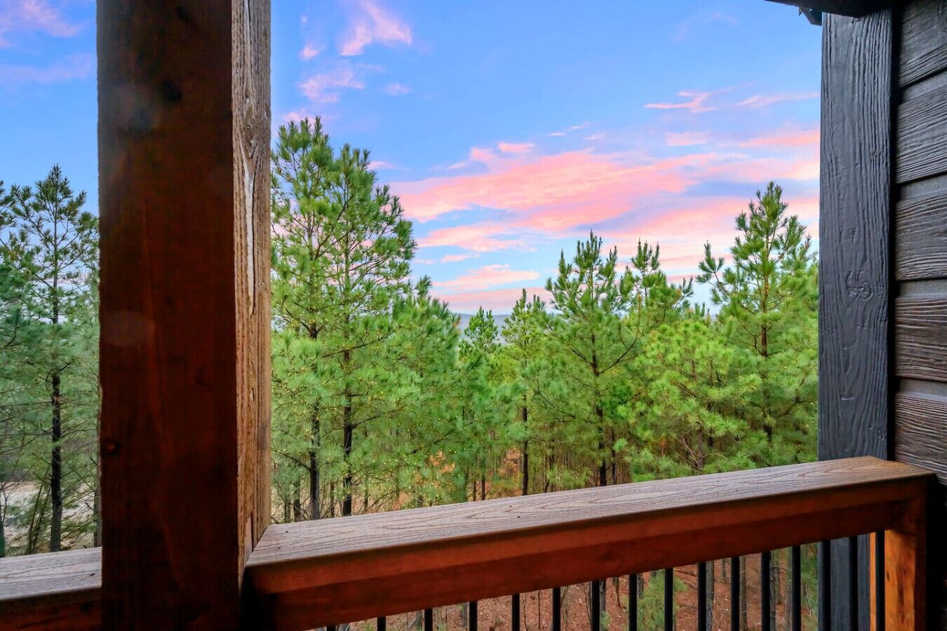A wooden deck with a view of a forest and a sunset sky.