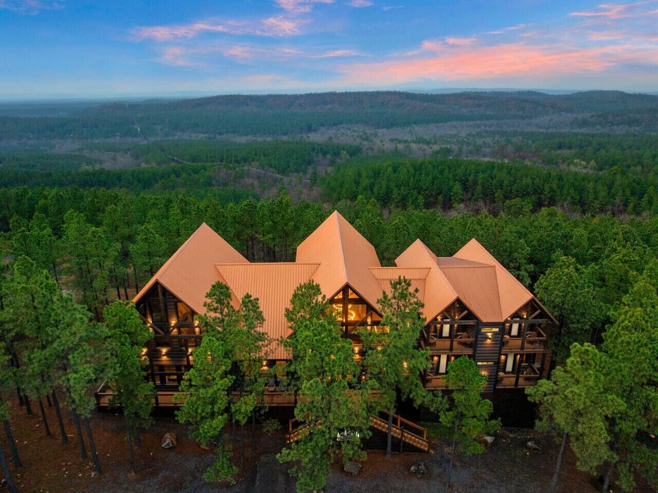 A multi-story lodge with a symmetrical roof design, surrounded by dense forest.