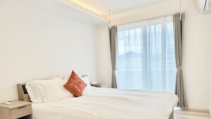 Een moderne slaapkamer met een groot bed, een nachtkastje en een raam met gordijnen.