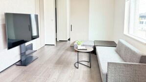Een moderne woonkamer met een flatscreen televisie, een bank, een klein rond tafeltje en een raam met uitzicht op de straat.
