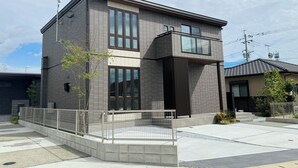 Um edifício moderno de dois andares com telhado plano, janelas grandes e entrada com portão.