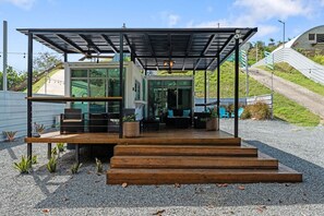 Een modern buitenzitgedeelte met een houten terras, glazen wanden en een metalen dak.