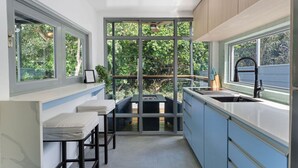 Una cocina moderna con un amplio ventanal, taburetes de bar y un lavabo.