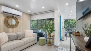 Una sala de estar moderna con un sofá, un espejo redondo, una planta en maceta y un televisor.