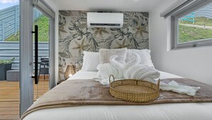 Un dormitorio con cama, aire acondicionado de pared, ventana y vistas al exterior.