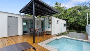 Una casa moderna frente al mar con piscina, mobiliario exterior y un porche cubierto.
