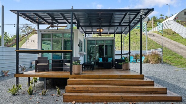 Un área de estar moderna al aire libre con un porche cubierto y escalones que conducen a ella, con vistas al paisaje circundante.