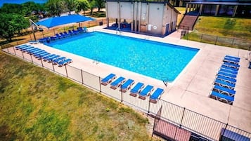 Een rechthoekig zwembad met blauwe ligbedden eromheen, een overdekte zithoek en een gebouw met een overdekt terras.