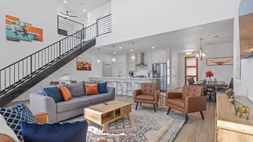 A spacious living area with a grey sofa, brown armchairs, and a wooden coffee table. A staircase with a black railing leads to an upper level.