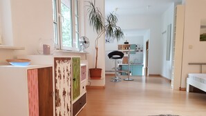 A modern interior with a wooden floor, a white reception desk, a potted plant, and a kitchen in the background.