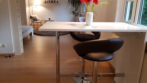 A modern kitchen with a white countertop, a vase with red flowers, and a black chair.