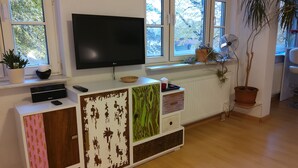 A living room with a TV, a cabinet with drawers, a radiator, and a window with a view of trees.
