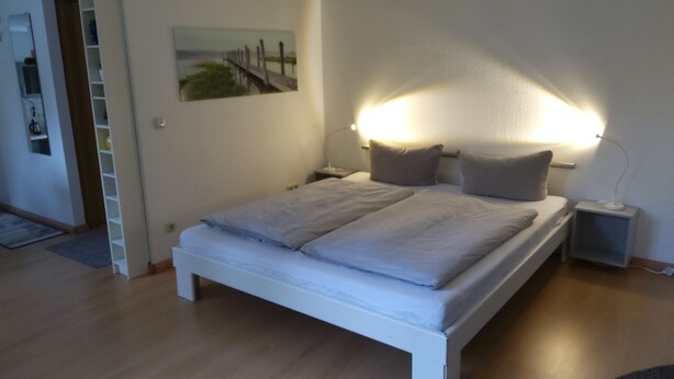 A bedroom with a bed, bedside tables, a nightstand, a wall-mounted lamp, and a painting on the wall.