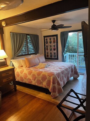 Ein Schlafzimmer mit Bett, Deckenventilator, Fenster mit Vorhängen, einer Wanddekoration mit Ananas und einem Balkon.