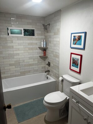 Ein Badezimmer mit Badewanne, Toilette und Waschbecken, mit Regalen für Toilettenartikel und gerahmten Bildern an der Wand.
