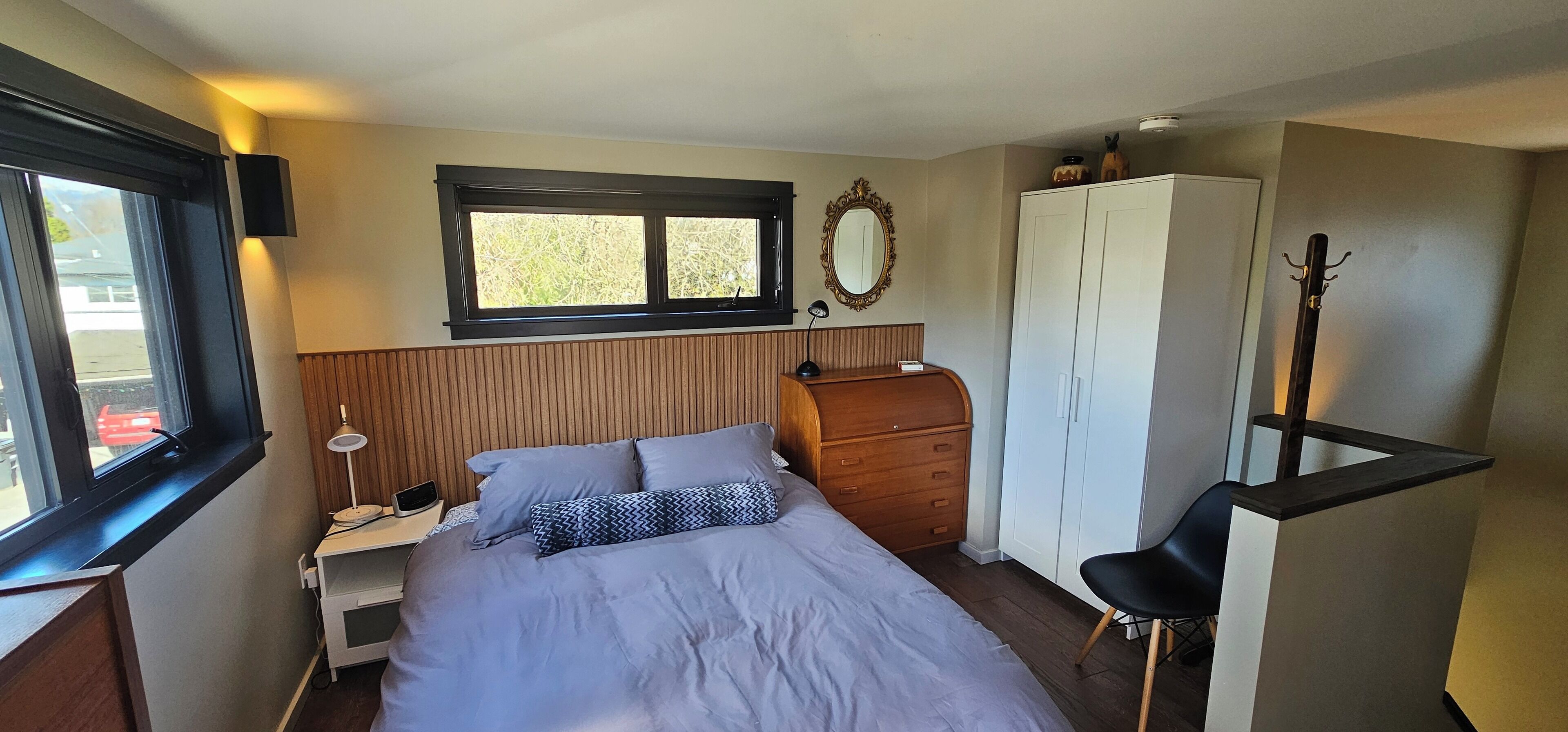 Une chambre à coucher comprenant un lit, une armoire, un bureau avec une lampe, une chaise et un porte-manteau.