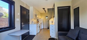 A compact kitchen with white appliances, a dining area with a bench, and a sofa. - Trout Lake Vancouver Urban Coach House (Vancouver)