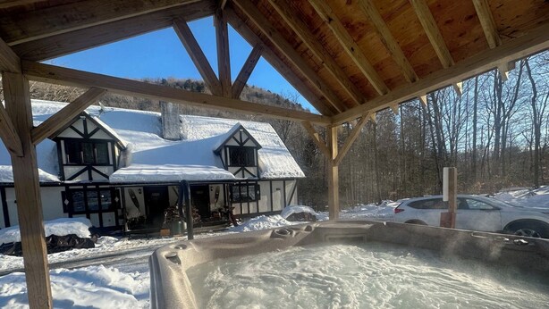Een hottub onder een houten pergola, met een besneeuwd gebouw op de achtergrond.