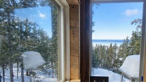 Une cabane en bois avec une fenêtre donnant sur une forêt enneigée et un ciel dégagé.