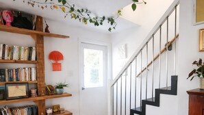 Un escalier avec des rampes noires, une bibliothèque en bois remplie de livres, une plante en pot et un objet décoratif rouge accroché au mur.