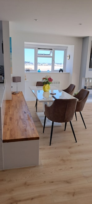 A modern kitchen with a dining area, featuring a wooden countertop, a glass table, and brown chairs.