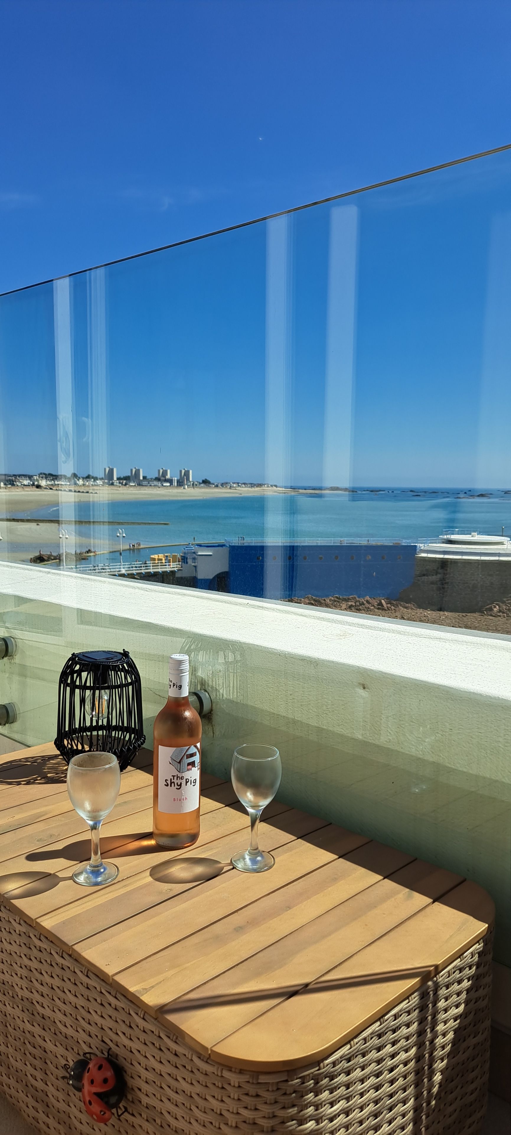A table with a bottle and two glasses, overlooking a beach and ocean.