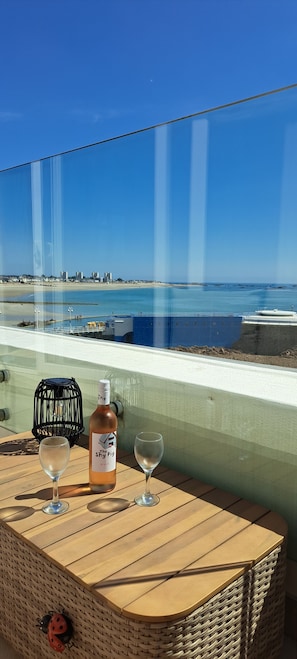 A table with a bottle and two glasses, overlooking a beach and ocean.