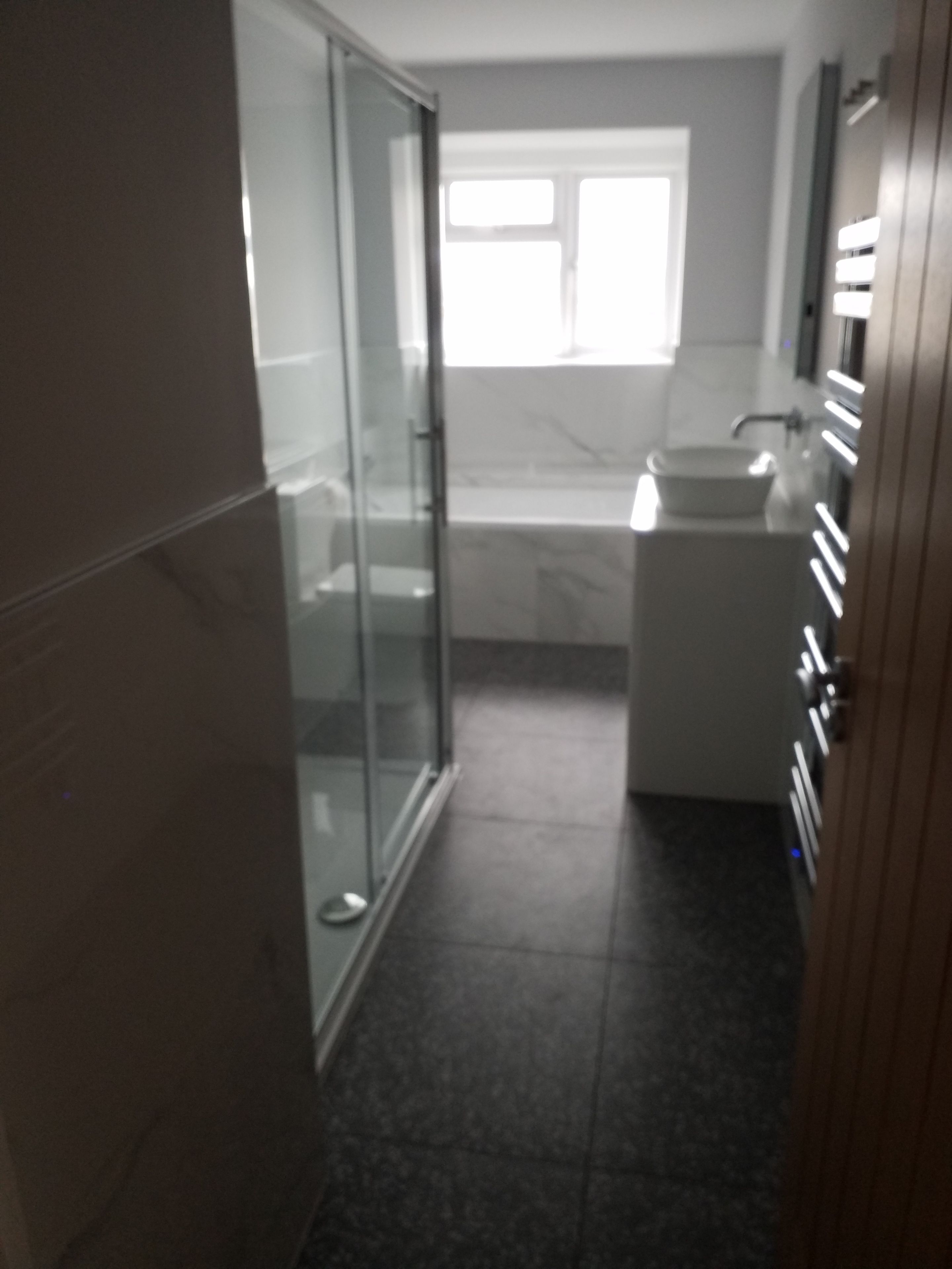 A bathroom with a glass shower enclosure, a sink, and a window providing natural light.