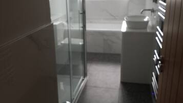 A bathroom with a glass shower enclosure, a sink, and a window providing natural light.
