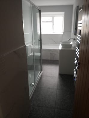 A bathroom with a glass shower enclosure, a sink, and a window providing natural light.