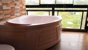 A bathroom with a large bathtub, a toilet, and a window with a view of greenery.