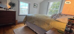 Une chambre à coucher avec un lit, une commode, des fenêtres et une lampe.