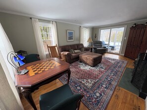 Un salon avec une table d’échecs, un canapé, un tapis à motifs et une vue sur l’extérieur, visible à travers une porte vitrée.